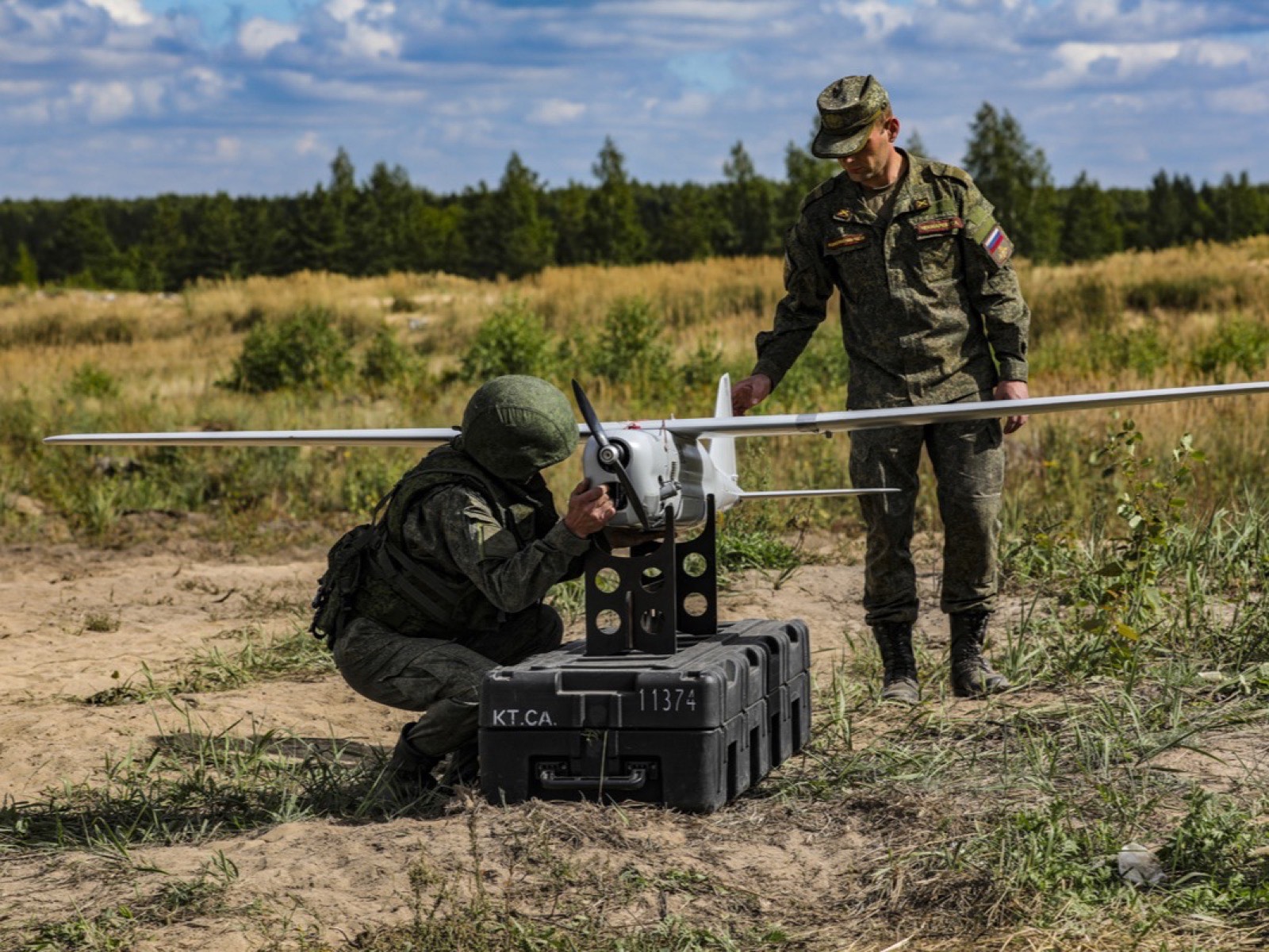 Два военнослужащих у беспилотника «Орлан-10» на стойке на транспортном кейсе: один осматривает аппарат, второй стоит рядом